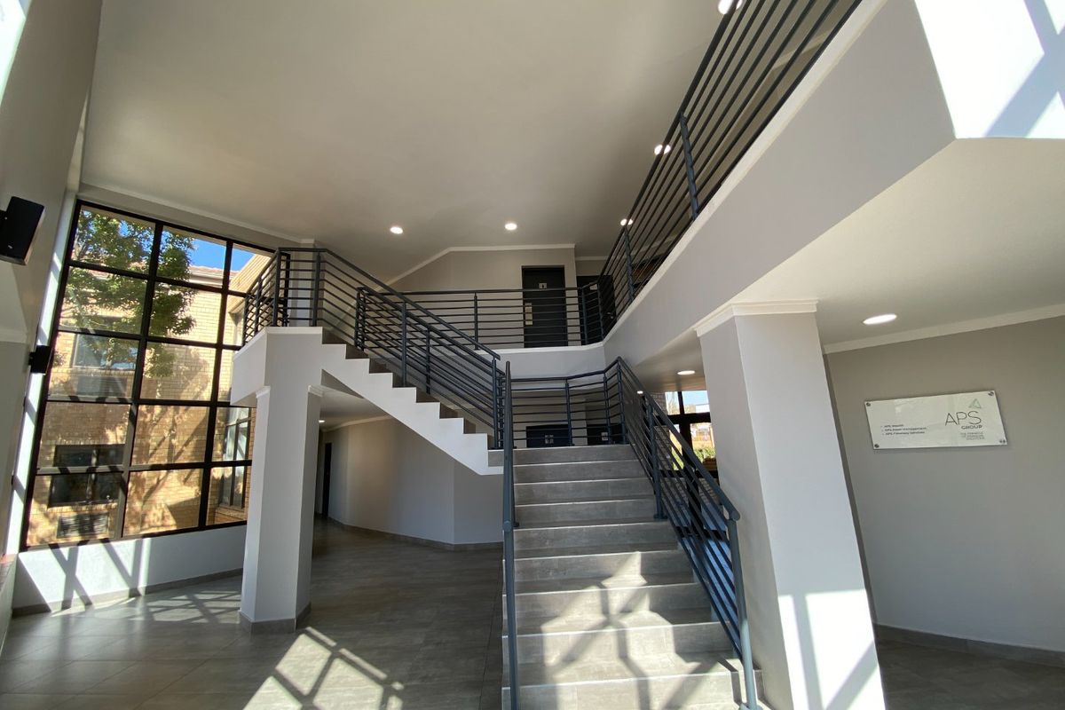 Spacious commercial building entrance featuring a modern staircase with metal balustrades, large windows, and clean tiled flooring.
