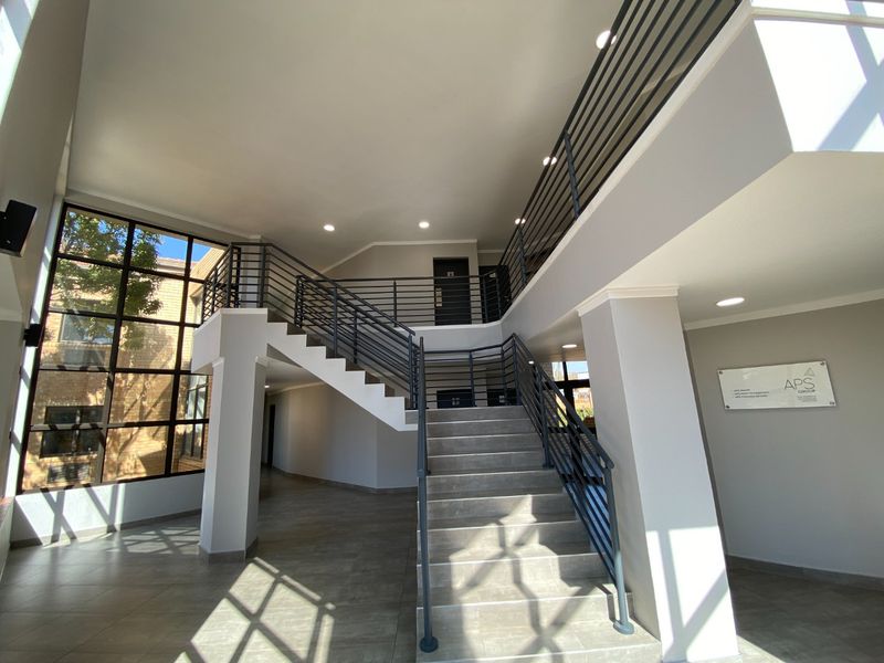 Spacious commercial building entrance featuring a modern staircase with metal balustrades, large windows, and clean tiled flooring.