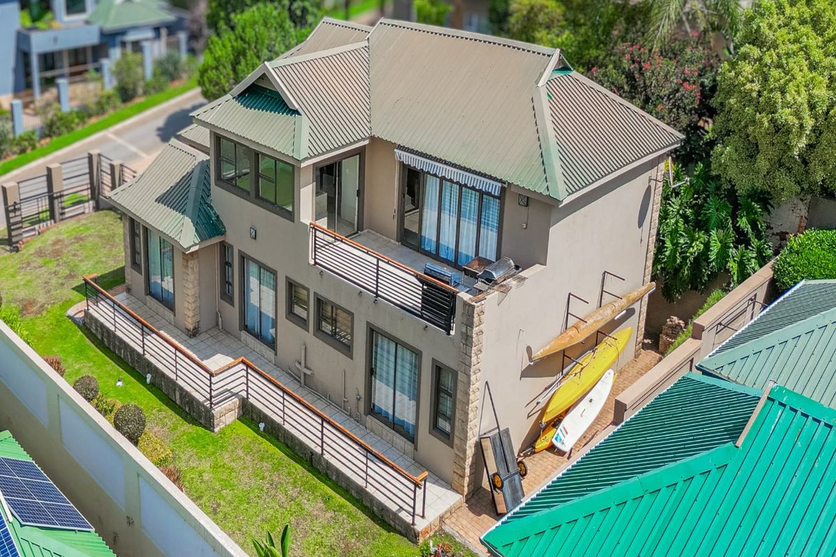Aerial view of a two-story residential property featuring a metal roof, balcony, and paved patio area within a landscaped garden setting.