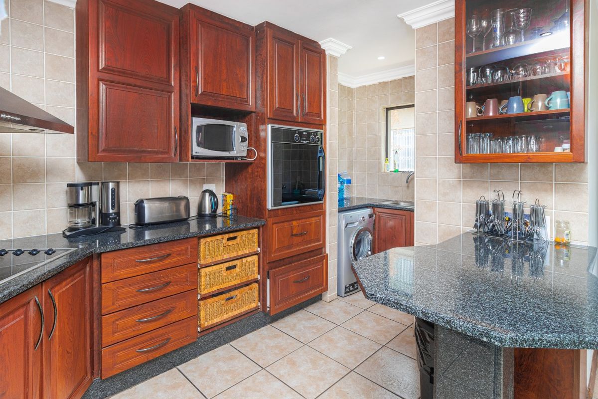 A functional kitchen featuring dark wood cabinetry, granite countertops, built-in oven, and a tiled backsplash, with an adjoining scullery area visible.
