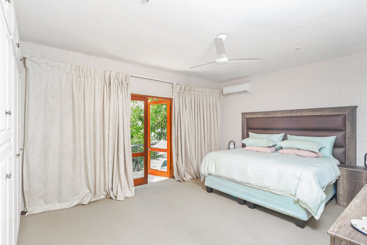 Spacious bedroom featuring neutral carpeting, built-in wardrobes, a ceiling fan, air conditioning, and direct access to an outdoor area through timber-framed glass doors.