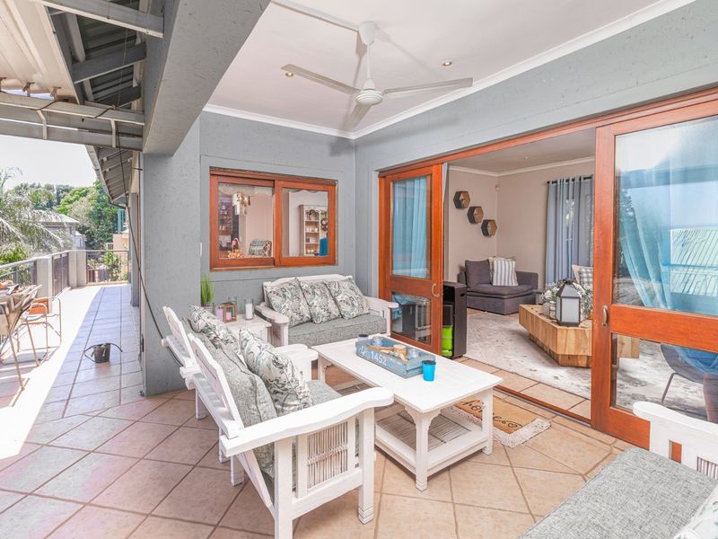 A covered patio area featuring tiled flooring, a ceiling fan, and large sliding glass doors providing seamless access to the interior living space.