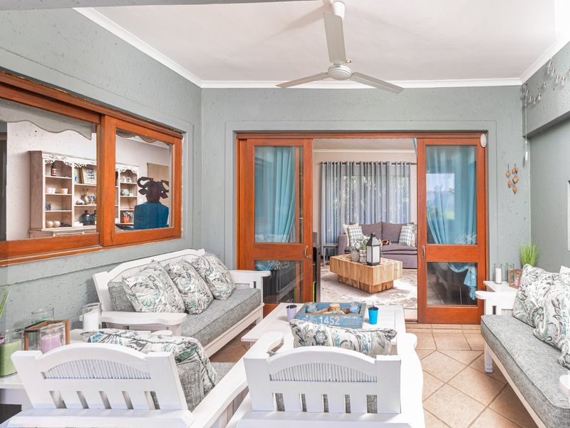 A covered patio area featuring tiled flooring, a ceiling fan, and timber-framed sliding doors providing access to the interior living space.
