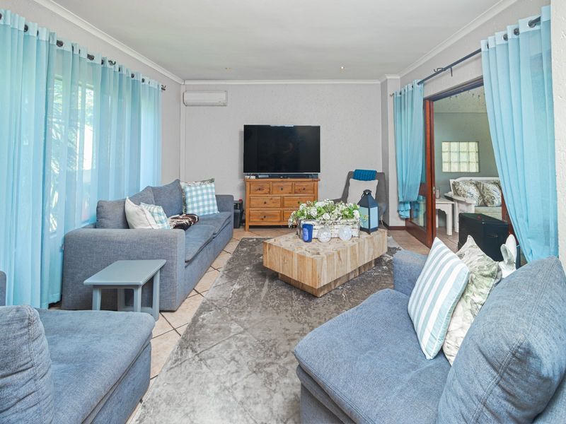 A comfortable living room featuring tiled flooring, a wall-mounted air conditioning unit, and direct access to an adjacent space through sliding glass doors.