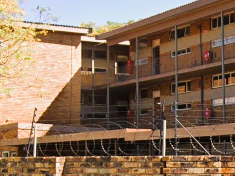 Multi-story commercial or residential brick building featuring external walkways, metal railings, and perimeter security fencing with razor wire.