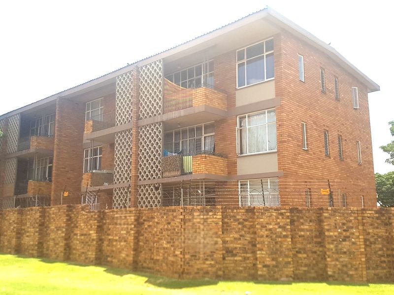 A multi-story commercial or residential brick building featuring decorative breeze block screens, private balconies, and a secure perimeter wall with razor wire fencing.