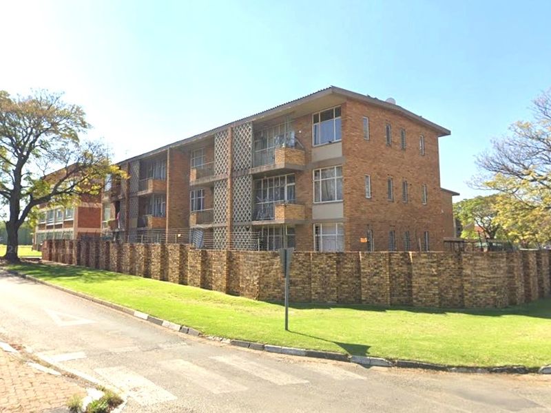 A multi-story commercial or residential brick building featuring private balconies, enclosed by a perimeter brick wall and security fencing in a street-facing setting.