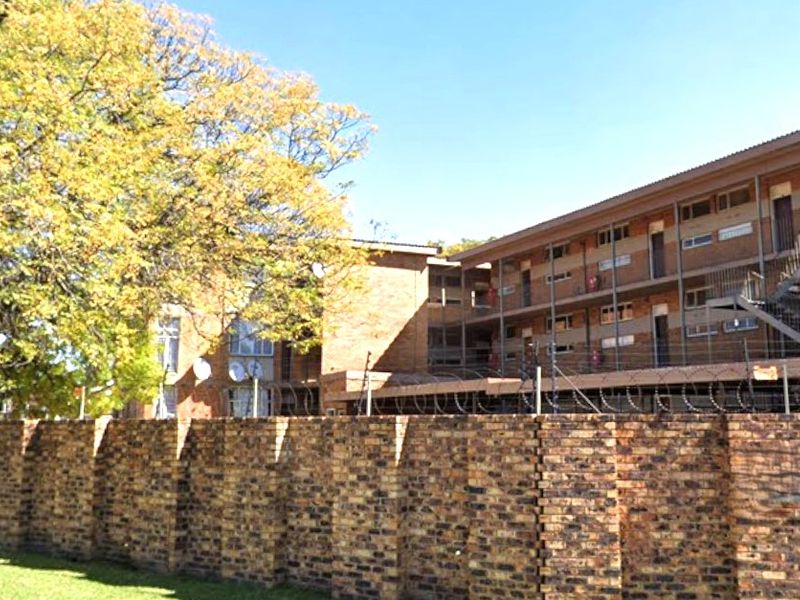 Exterior view of a multi-story commercial or residential brick building featuring external steel staircases and secure perimeter fencing with razor wire.