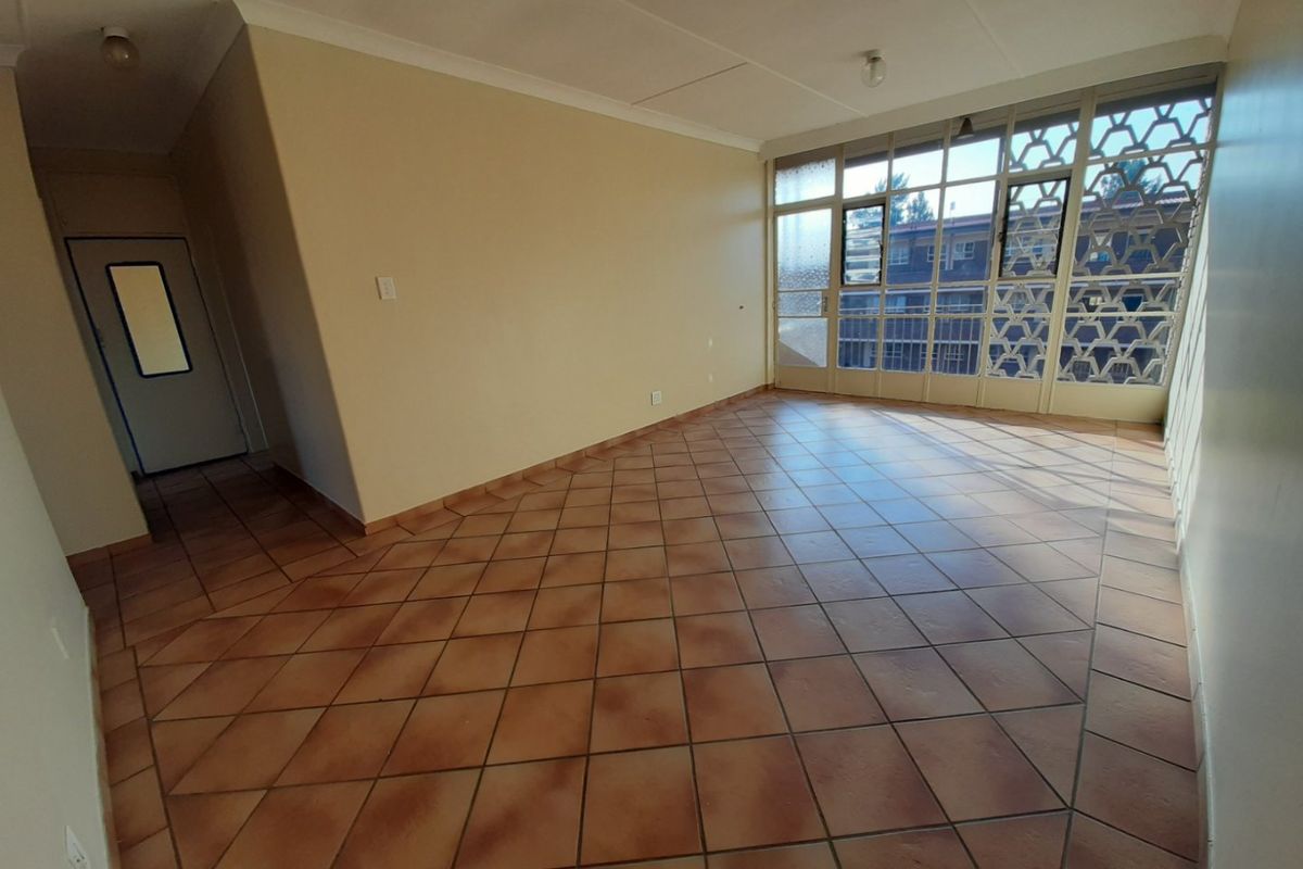 An empty, open-plan living area featuring terracotta-style floor tiles, large windows with decorative metal screens, and neutral wall finishes.