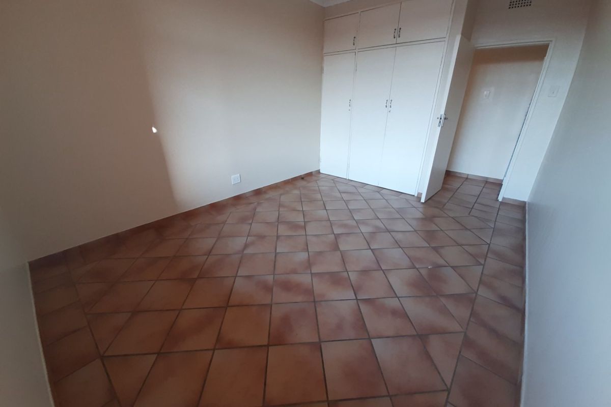 An empty bedroom featuring tiled flooring and built-in cupboards, providing a clean and neutral space ready for customization.