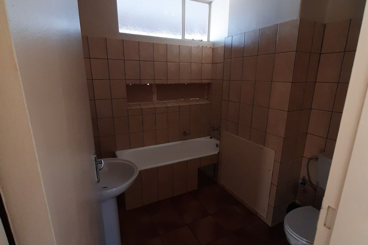 A dated bathroom featuring a pedestal basin, built-in bathtub, and toilet, finished with brown ceramic wall and floor tiles.