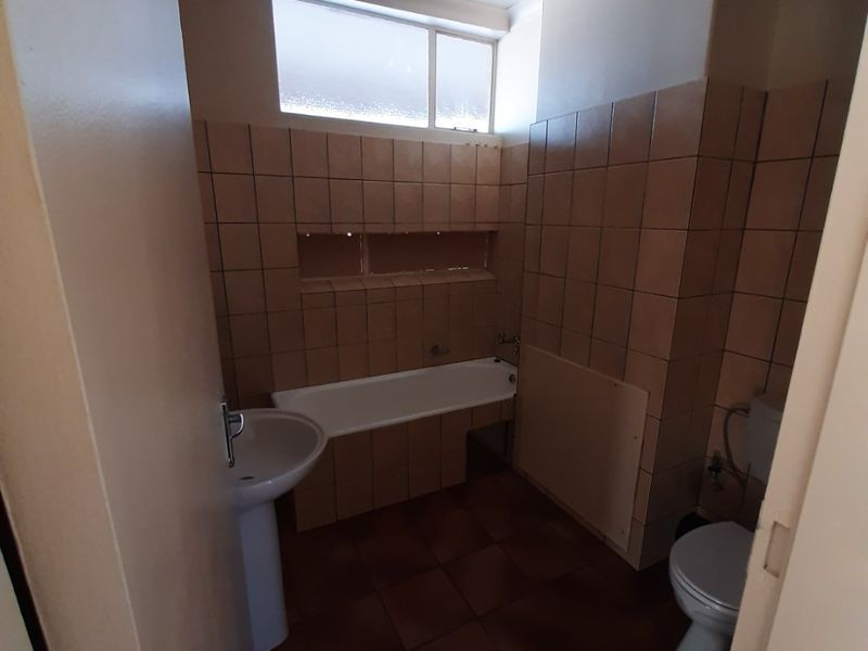 A dated bathroom featuring a pedestal basin, built-in bathtub, and toilet, finished with brown ceramic wall and floor tiles.
