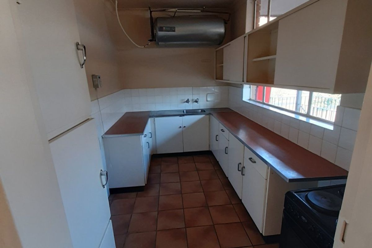 A functional kitchen featuring tiled flooring, built-in cabinetry, laminate countertops, and a wall-mounted electric geyser, offering a practical layout for renovation.