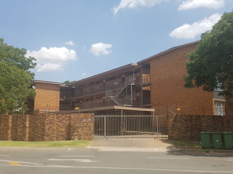 Street view of a multi-story commercial or residential brick building featuring a secure gated entrance, electric fencing, and external stairwell access.