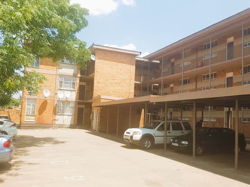 Exterior view of a multi-story commercial or residential brick building featuring covered parking bays and external access staircases.