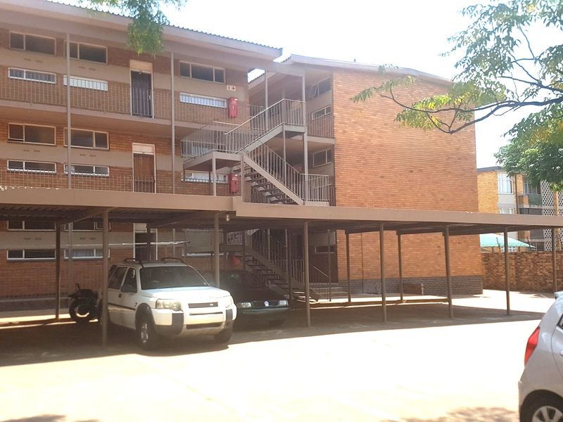 Exterior view of a multi-story commercial apartment building featuring brick facade, external metal staircases, and covered parking bays.