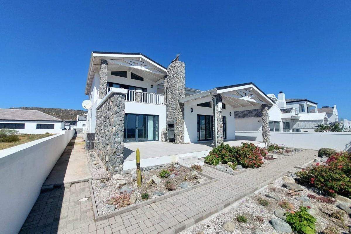 Rear view of a modern house featuring stone cladding, a covered patio with a built-in braai, and an upper-level balcony.