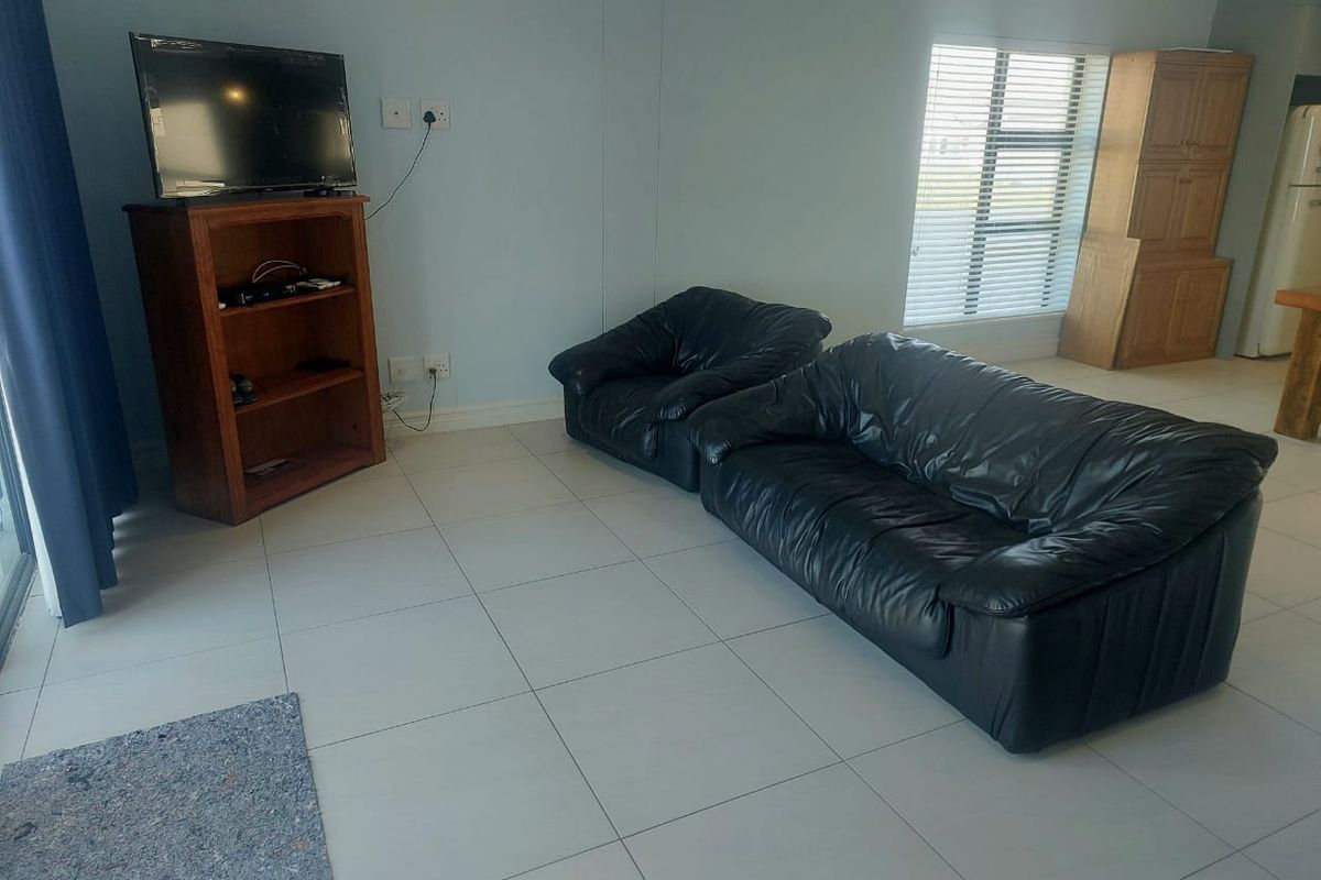 A living area featuring light-colored floor tiles, a wall-mounted air conditioning unit, and large windows with venetian blinds.