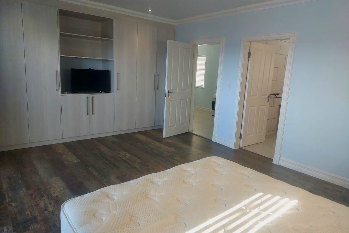 Spacious bedroom featuring extensive built-in cabinetry, modern laminate flooring, and direct access to an en-suite bathroom.