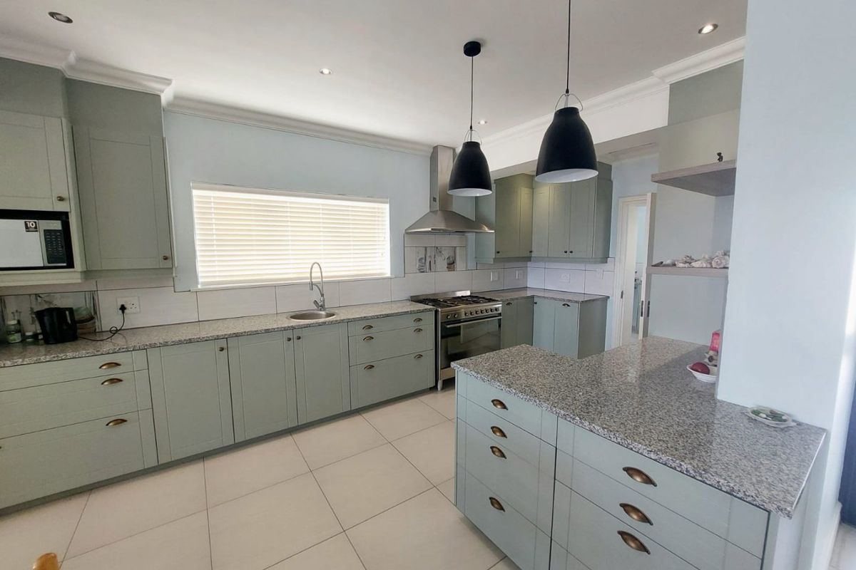 Modern kitchen featuring sage green cabinetry, granite countertops, stainless steel appliances, tiled flooring, and a functional island layout with ample storage.