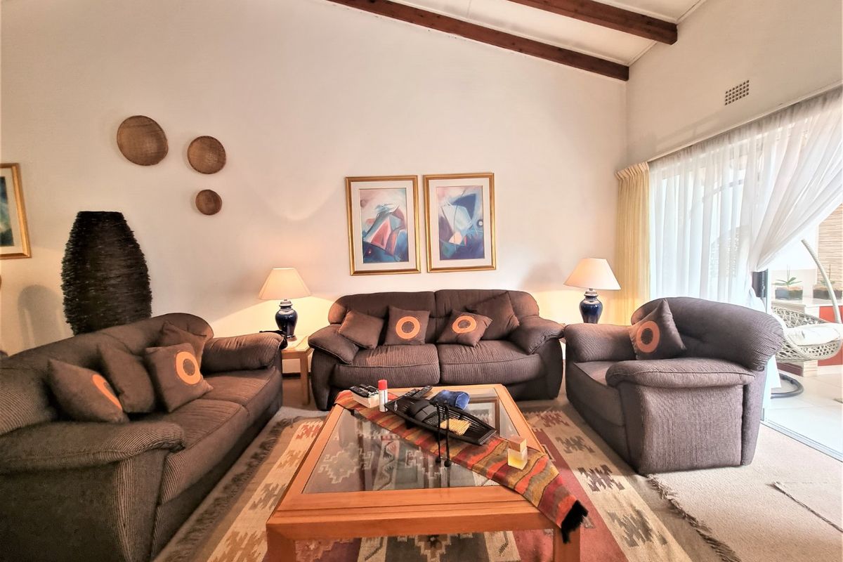 A spacious living room featuring high vaulted ceilings with exposed timber beams and large sliding glass doors providing access to the patio.