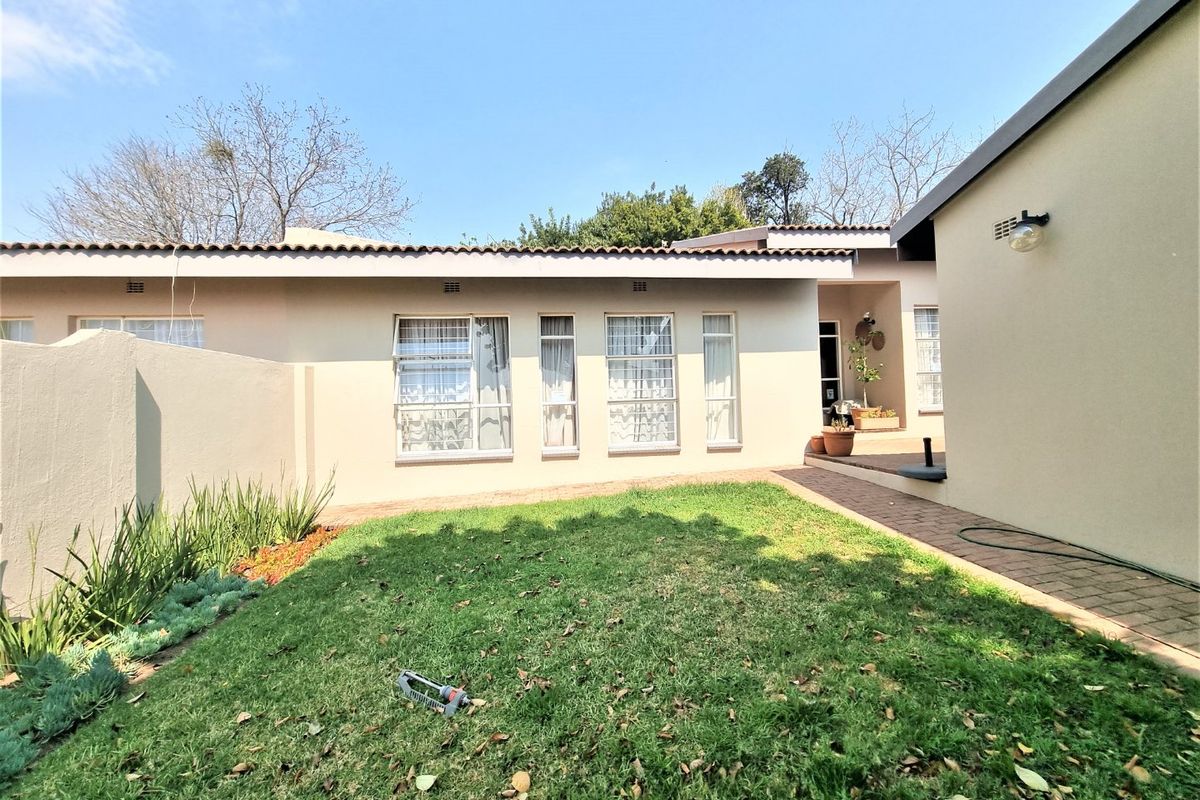 A well-maintained rear exterior view of the townhouse featuring a paved walkway, lawn area, and neutral-toned facade with aluminium window frames.