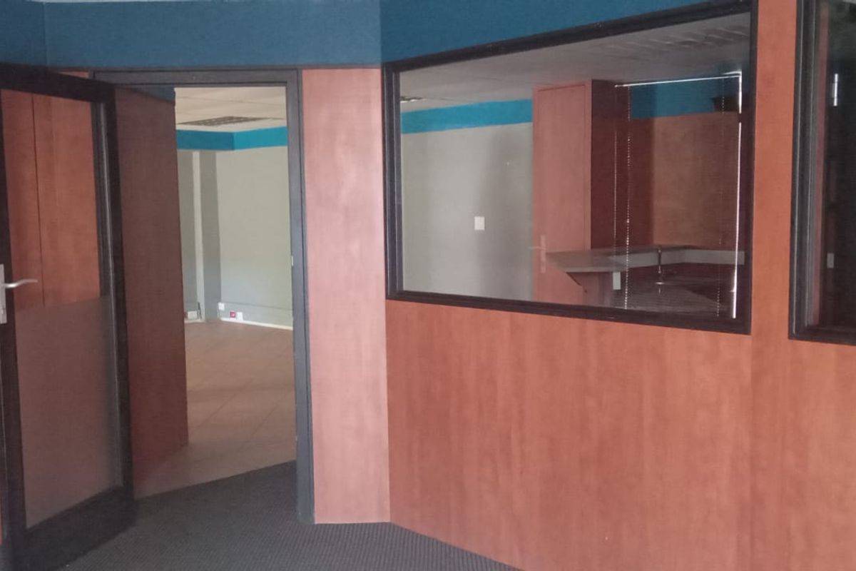 An empty commercial office space featuring wood veneer wall paneling, glass partitions, and carpeted flooring, suitable for a professional workspace layout.