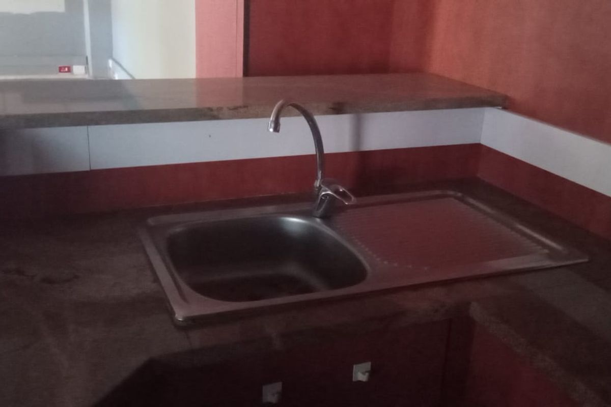 A basic kitchen prep area featuring a stainless steel sink, stone countertop, and visible electrical outlets, currently in need of cosmetic updates.