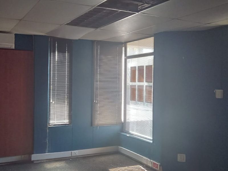 An empty commercial office space featuring a suspended ceiling, split-system air conditioning, and carpeted flooring, requiring maintenance and cosmetic updates.