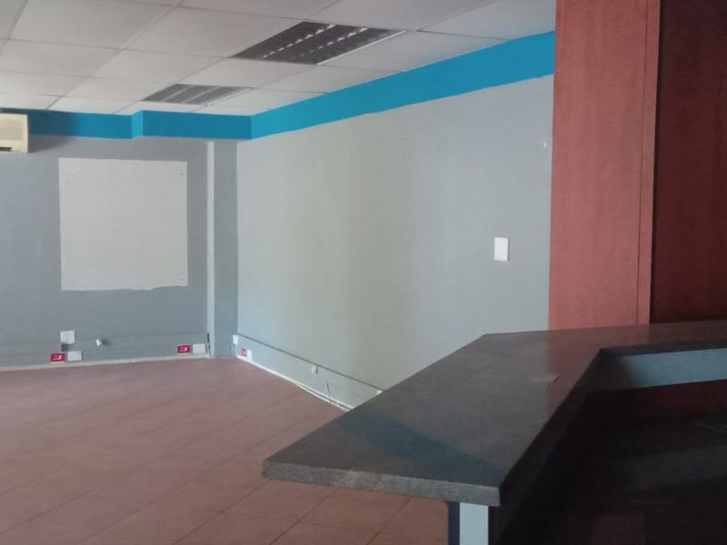 Open-plan commercial space featuring tiled flooring, a suspended ceiling with recessed lighting, a split-system air conditioner, and a built-in kitchenette area with a sink.
