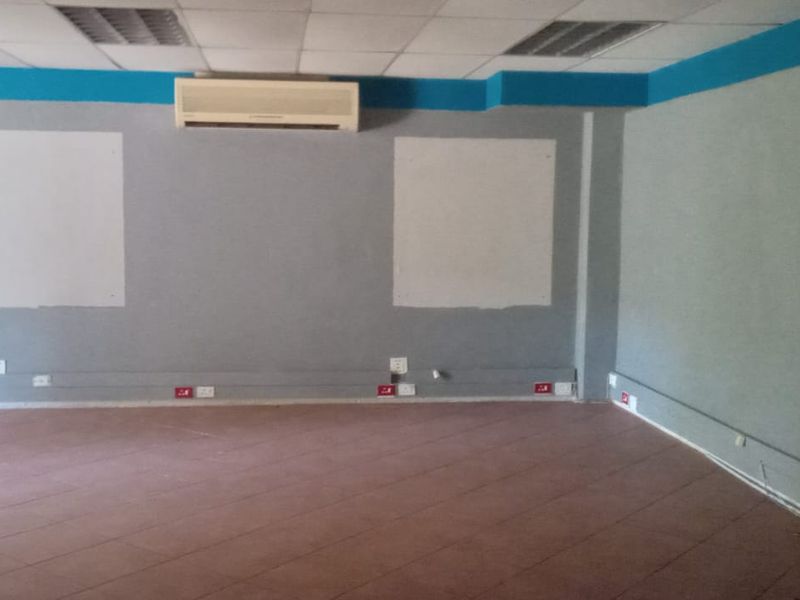 An empty commercial office space featuring tiled flooring, a suspended ceiling, wall-mounted air conditioning, and visible electrical trunking along the walls.