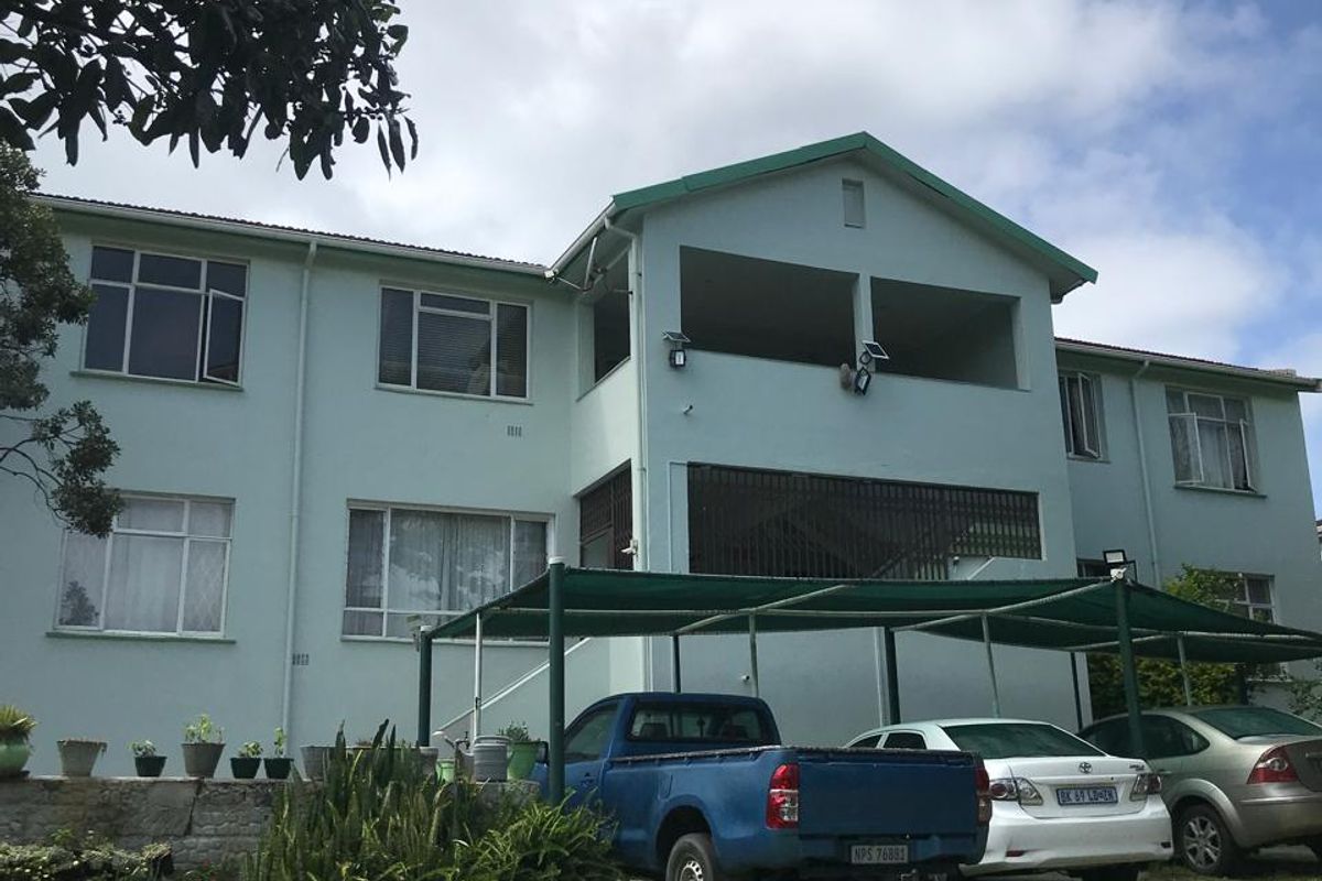 Rear view of a multi-story apartment building featuring a balcony, carport structure, and established garden area.