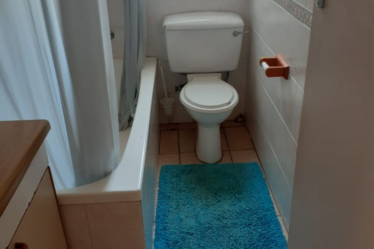 A compact bathroom featuring a bathtub, toilet, and vanity cabinet with dated wall and floor tiling, offering potential for a modern renovation.