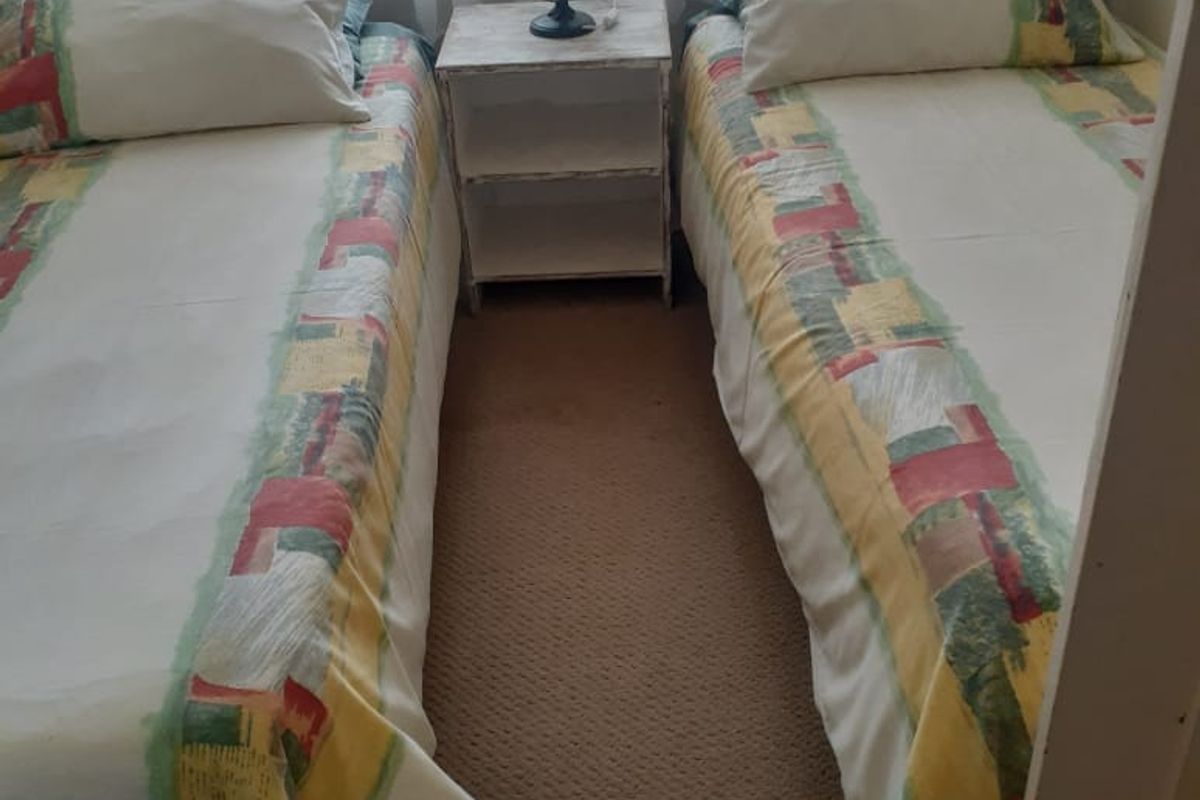 A compact bedroom featuring carpeted flooring and a window with natural light, currently configured with twin beds.