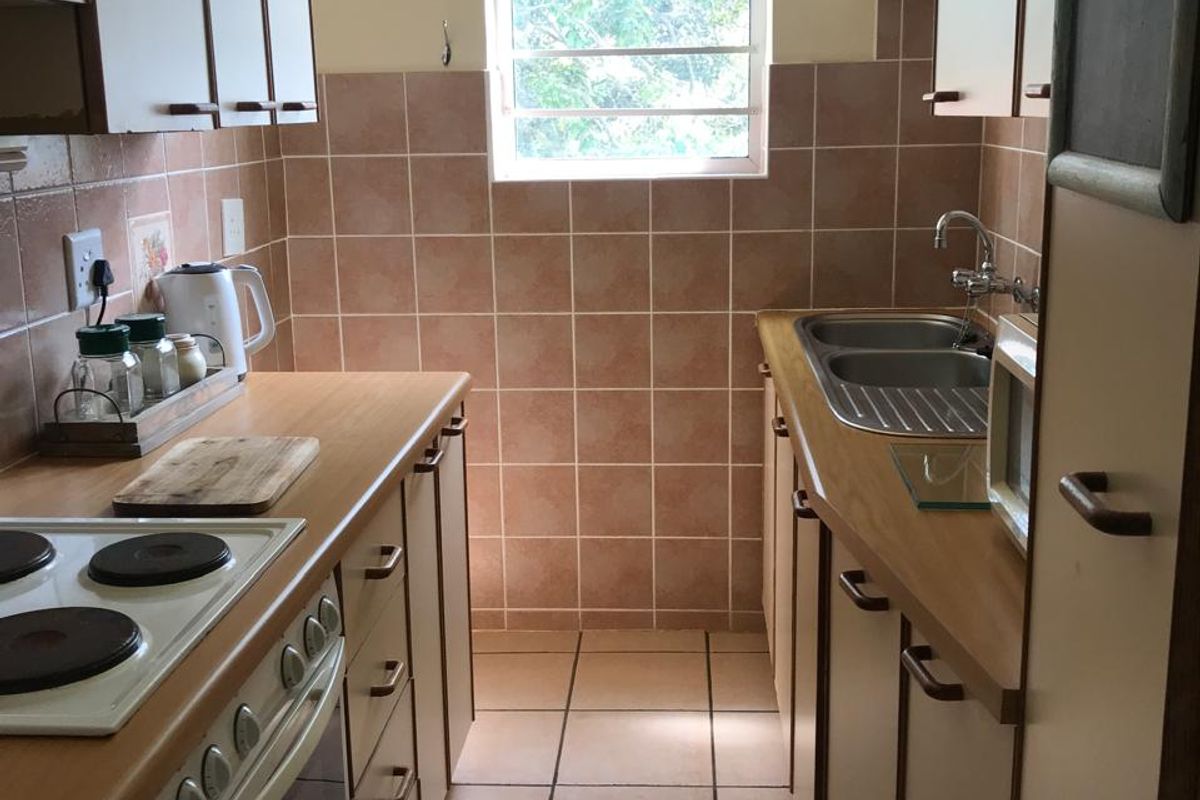 A compact galley-style kitchen featuring built-in cabinetry, laminate countertops, an electric stove, and a double basin sink with tiled backsplash and flooring.