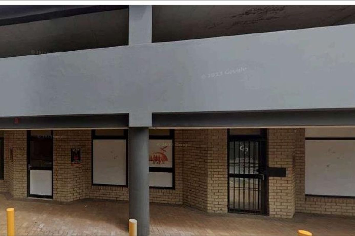 Front exterior view of a commercial building featuring a brick facade, concrete structural pillars, and secure entrance points with metal security gates.