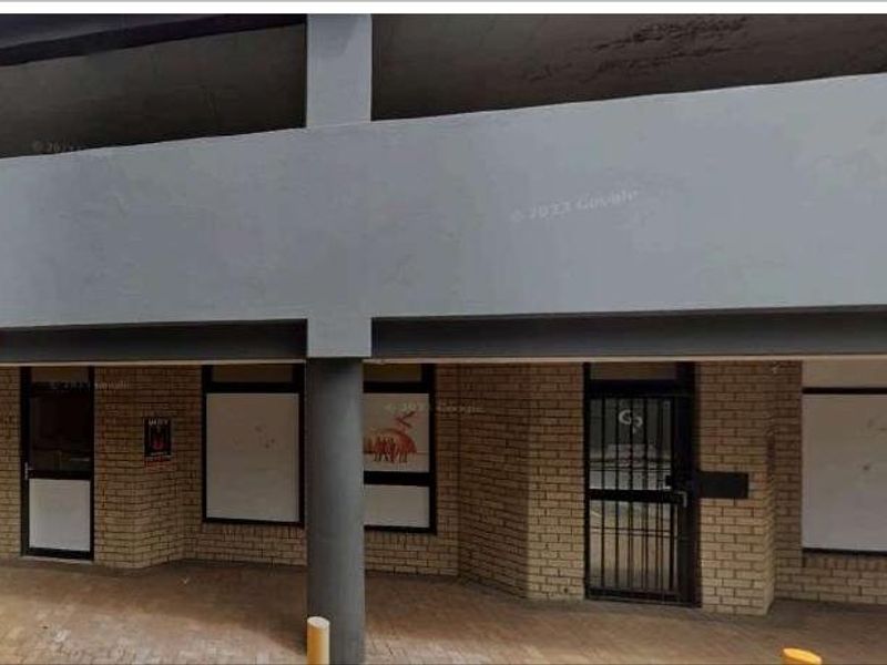 Front exterior view of a commercial building featuring a brick facade, concrete structural pillars, and secure entrance points with metal security gates.