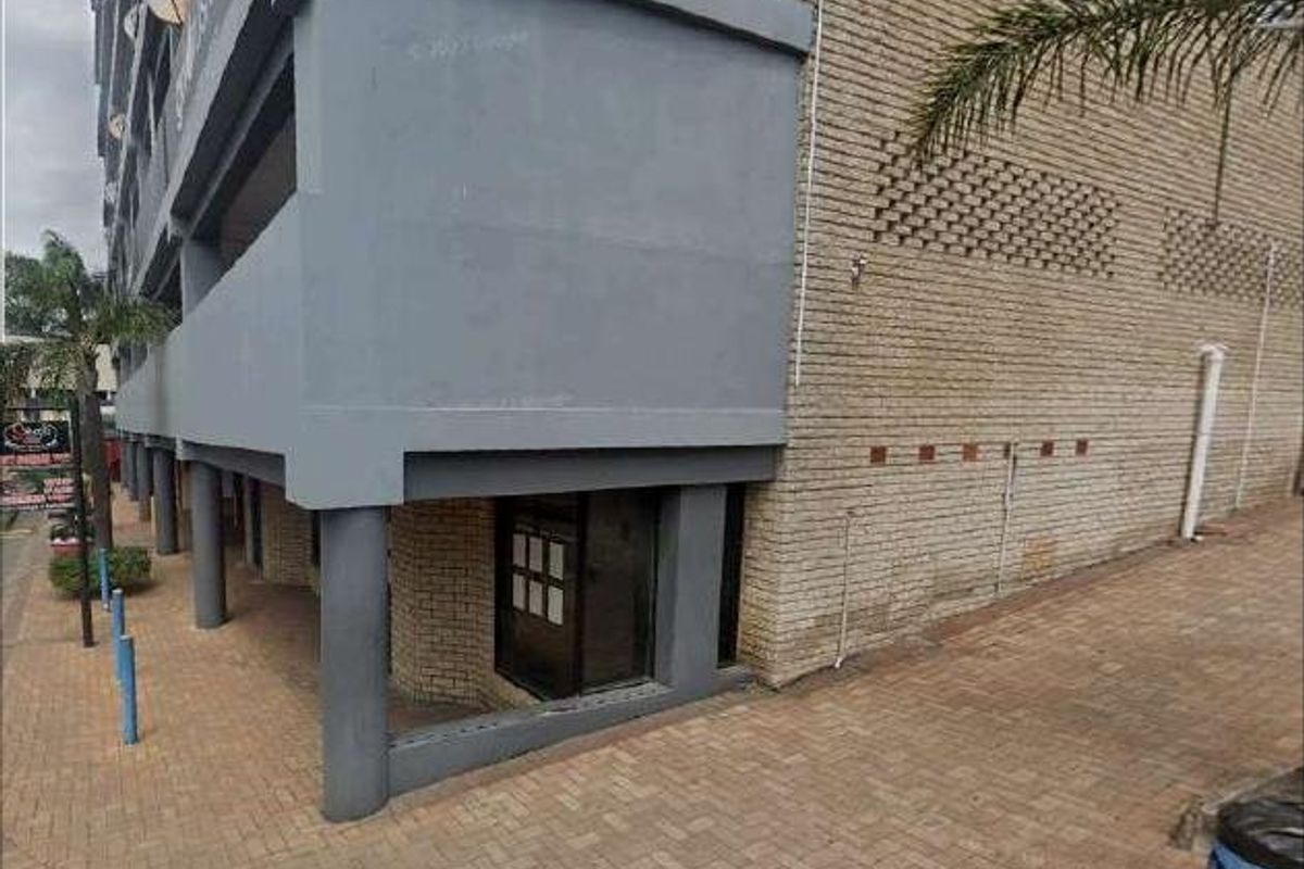 Exterior view of a commercial building featuring a brick facade, concrete support pillars, and a paved pedestrian walkway at the entrance.