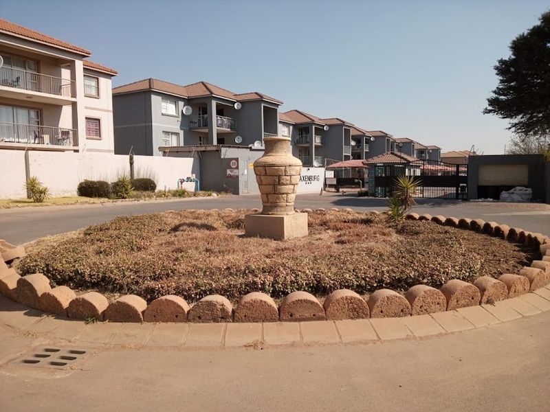 A view of the apartment complex entrance featuring a landscaped roundabout with a stone urn and secure gated access.
