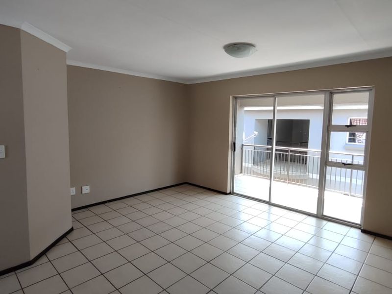 An empty, neutral-toned living room featuring tiled flooring and a large sliding glass door providing access to an outdoor balcony area.