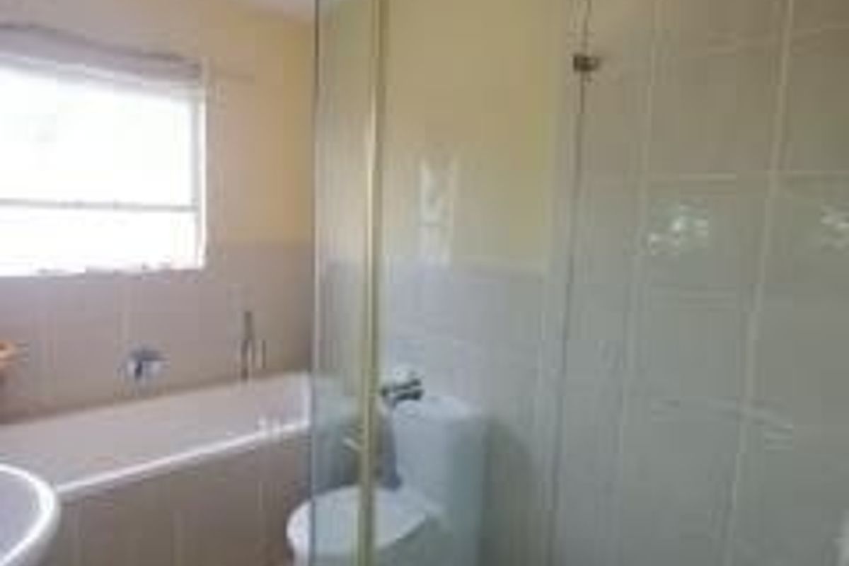 A functional bathroom featuring a built-in bathtub, a separate glass-enclosed shower, a pedestal basin, and neutral ceramic tiling throughout.