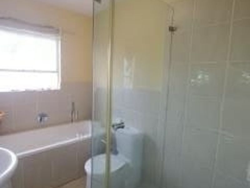 A functional bathroom featuring a built-in bathtub, a separate glass-enclosed shower, a pedestal basin, and neutral ceramic tiling throughout.