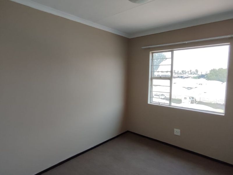 A clean, empty bedroom featuring neutral wall paint, carpeted flooring, and a window fitted with security bars.