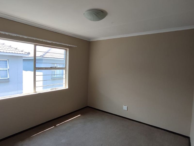 An empty bedroom featuring neutral wall paint, carpet flooring, and a window fitted with security bars.