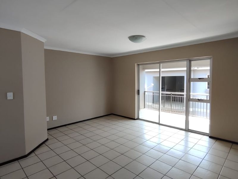 A bright, empty living room featuring neutral tiled flooring and a large sliding glass door providing access to an outdoor balcony area.