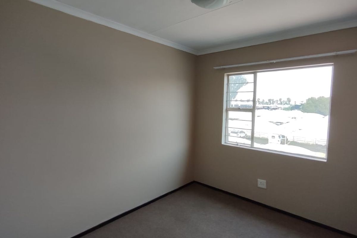 A clean, empty bedroom featuring neutral wall paint, carpeted flooring, and a window fitted with security bars.