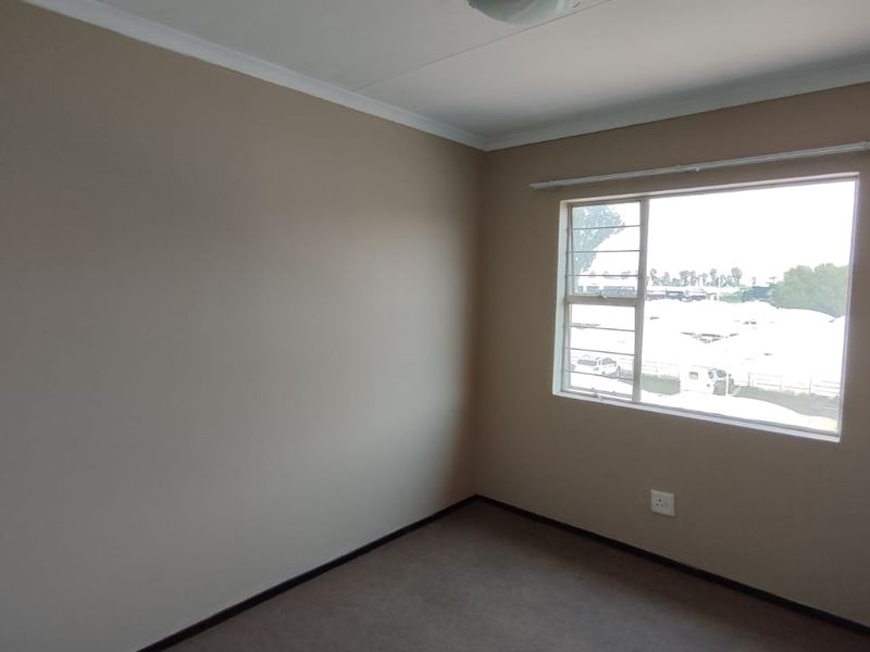 A clean, empty bedroom featuring neutral wall paint, carpeted flooring, and a window fitted with security bars.