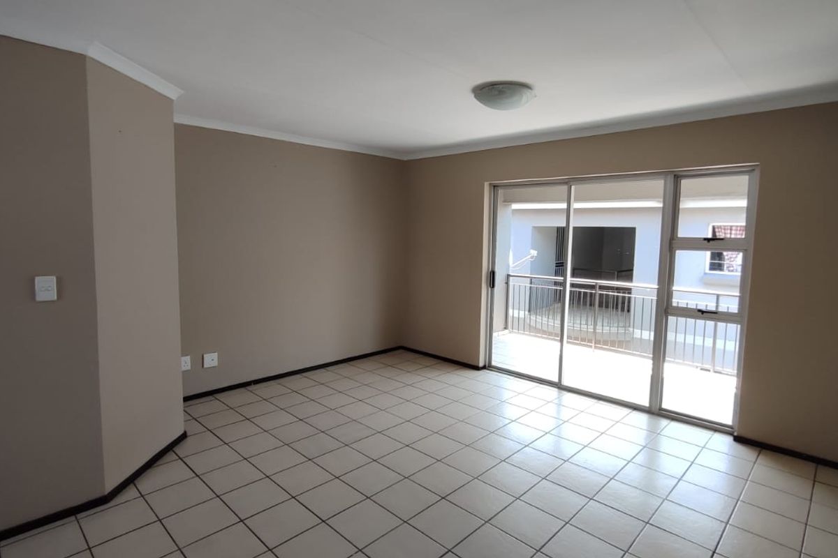 An empty, neutral-toned living room featuring tiled flooring and a large sliding glass door providing access to an outdoor balcony area.