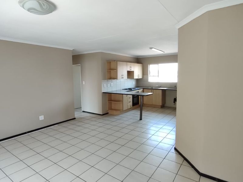 Open-plan living and kitchen area featuring tiled flooring, neutral wall tones, and functional built-in cabinetry with a breakfast bar.