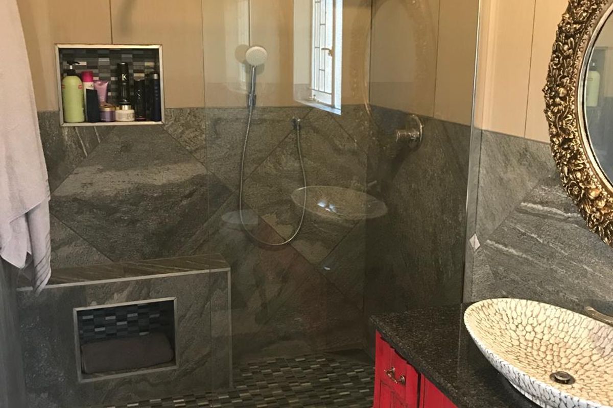 Modern bathroom featuring a walk-in shower with glass enclosure, stone-tiled walls, built-in shower niche, and a vanity with a vessel sink.